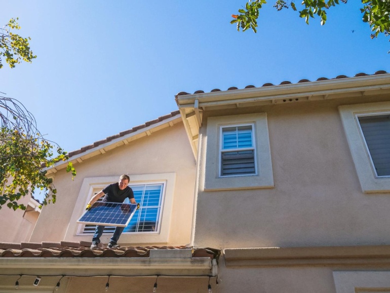 An image of a man holding a solar panel on the roof