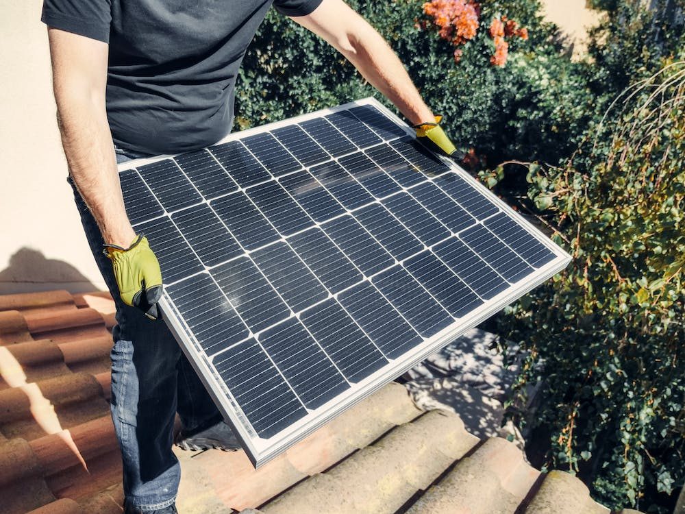 A Person in a Black Shirt Holding a Solar Panel while Standing on the Roof