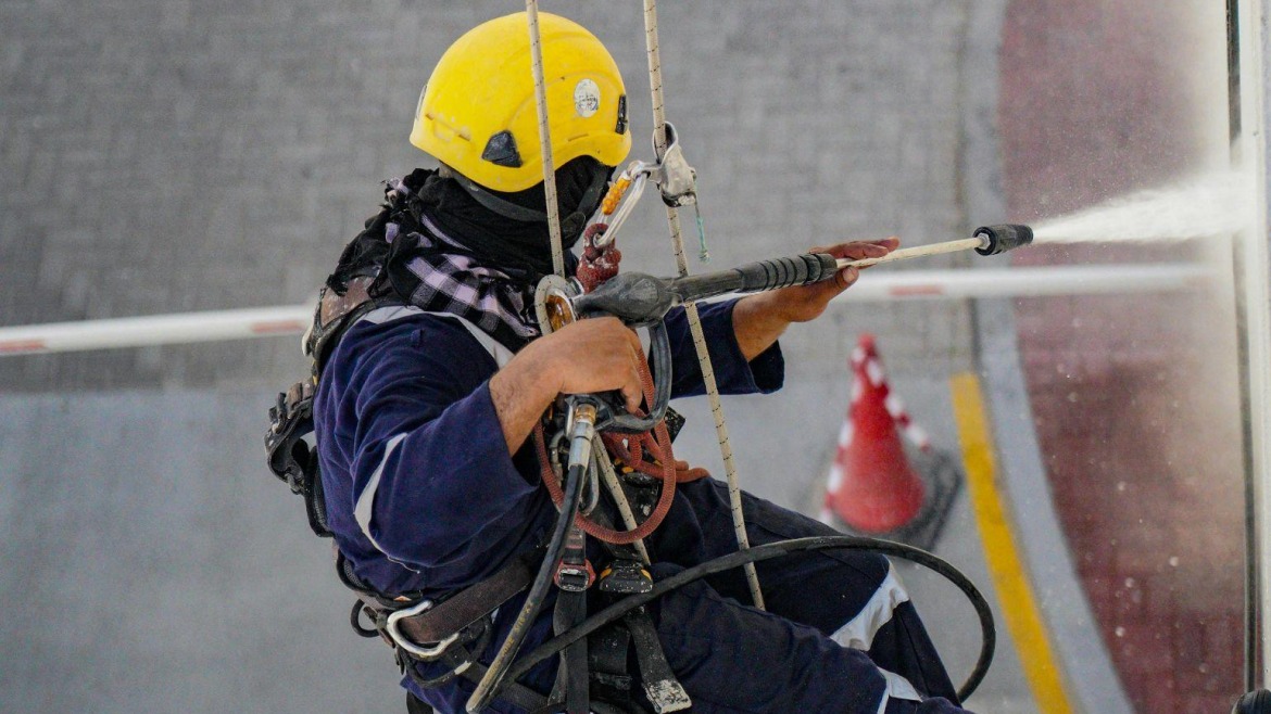 Worker in yellow helmet using a pressure washer on building exterior